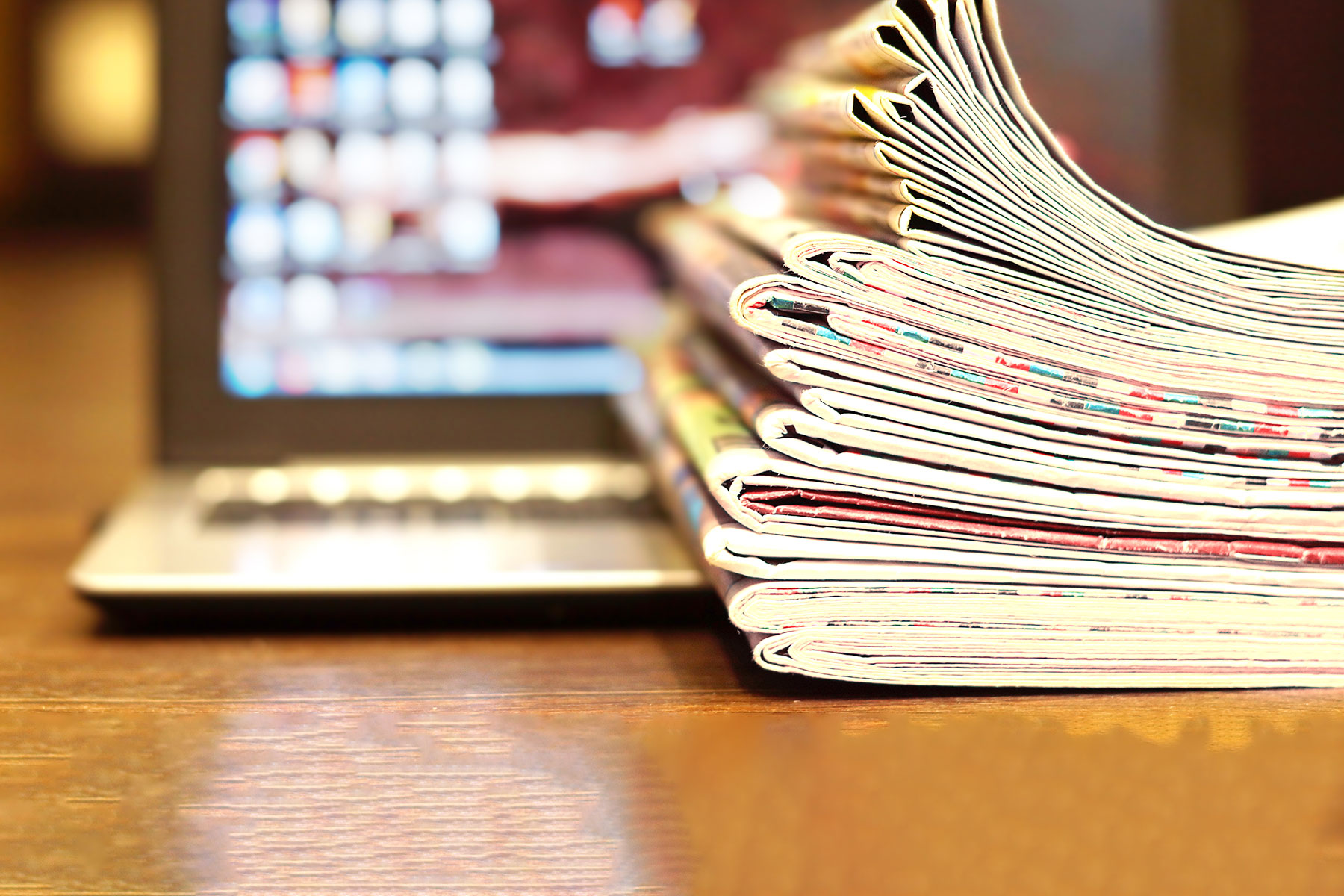journalism concept - close up of a large stack of newspapers and magazines sitting near a laptop