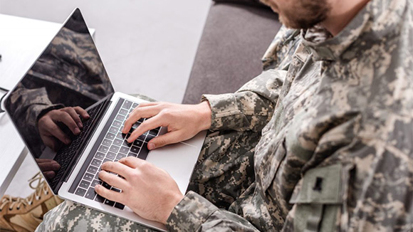 over the shoulder view of young man wearing military fatigues working on a laptop
