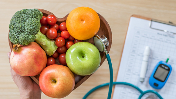 hearth shaped wooden bowl filled with fresh fruit and vegetables, a stethoscope sitting next to the bowl