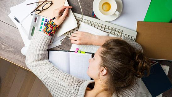 overhead view of an exhausted female student laying on top an array of a computer keyboard, notes, and books