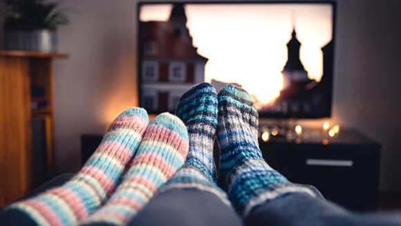 close up on a couples' feet covered in warm knitted slippers, in front of a tv screen