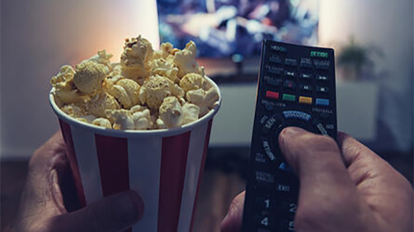 close up of a person holding a cup of popcorn and the tv remote