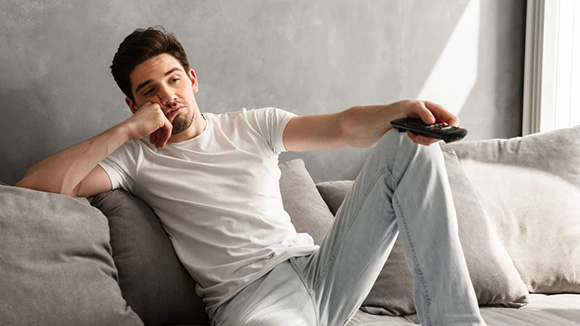 young male lounging on sofa holding tv remote