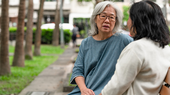 woman sitting on park bench talking with an older woman, possibly a mother and daughter