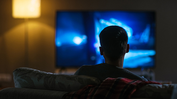 view of the back of a young man sitting on couch watching a movie on large television screen