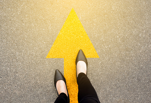 overhead shot of a woman's feet standing on asphalt with a painted arrow pointing upwards