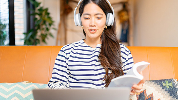 young female college student sits on a sofa with laptop in her lap wearing headphones