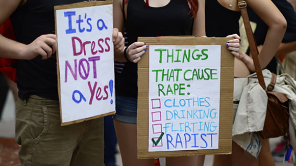 two young women during a protest or rally holding cardboard signs with anti sexual violence messages