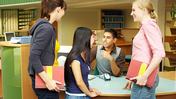 Students chatting while checking out books in library from a fellow student working