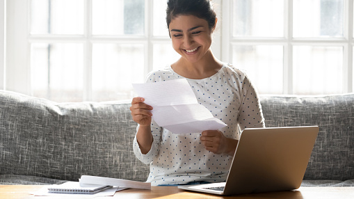 young woman sitting on couch opening a letter in the mail