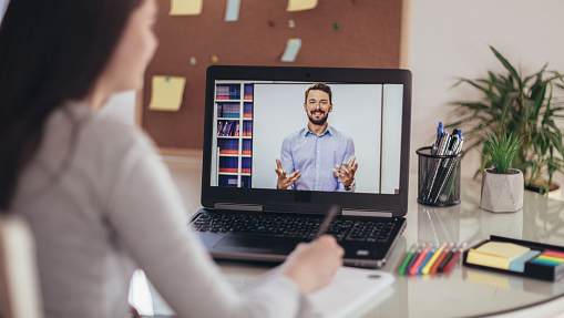 rear view of young woman on zoom call, focus on presenter on laptop