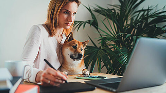 woman sitting at table, working on laptop with dog on her lap