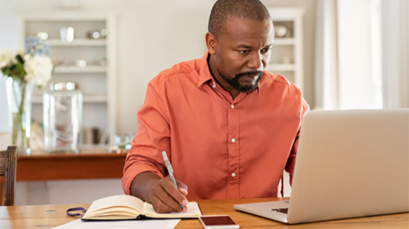 older man sitting at table at home working on laptop