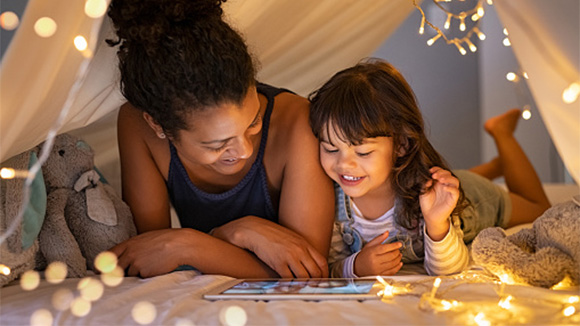 young black mom in a blanket fort with her daughter watching a show on an tablet in front of them