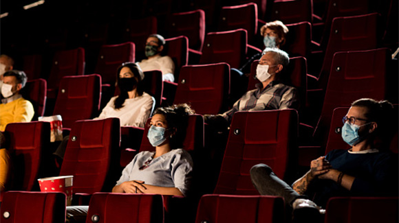 people watching a film in a movie theater during covid-19 pandemic as they're all wearing masks