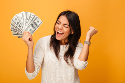 excited young woman holding dollar bills fanned out
