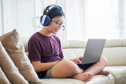 young boy sitting on couch playing game on laptop