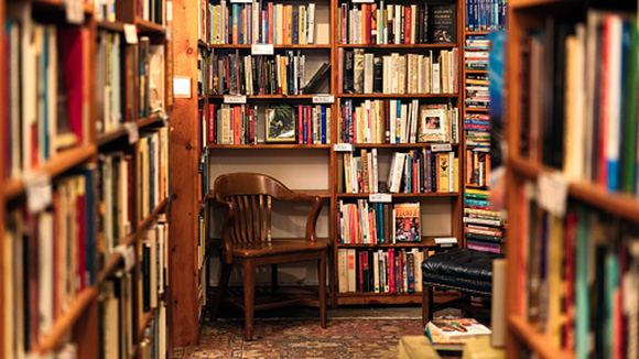 looking down a hall in a used bookstore, a lone wooden chair sitting in the corner