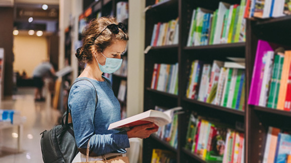 young woman in bookstore during covid-19 period as she's wearing a facemask