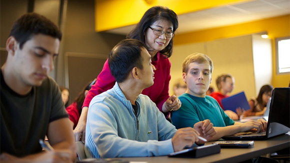 coastline college instructor lisa lee leans over the shoulders of two students to look at their work