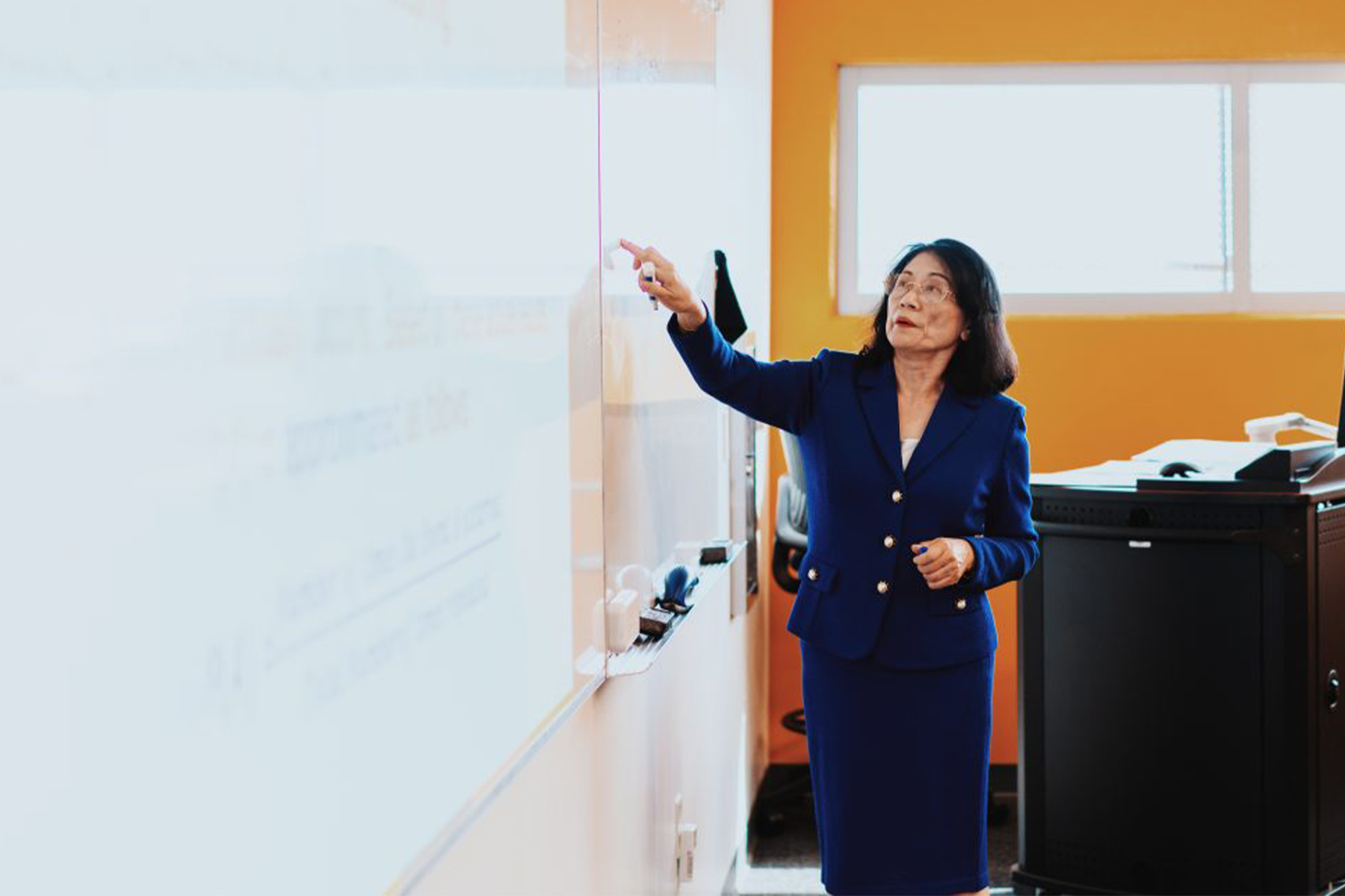 coastline professor Lisa Lee points at something on a white board as she instructs a class