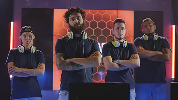 group of 4 male esports players standing amongst computers with serious expressions on their faces, looking intimidating
