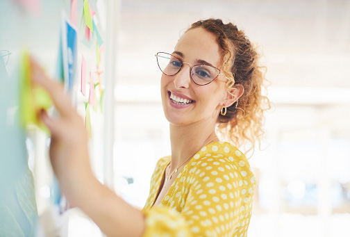 woman putting post-it notes on brainstorming white board