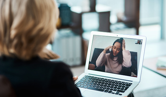 over shoulder view of a woman on laptop, viewing another young woman, seeming stressed, on a call