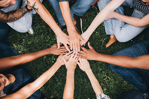 overhead view of diverse group of people sitting in a circle putting their hands together in the center