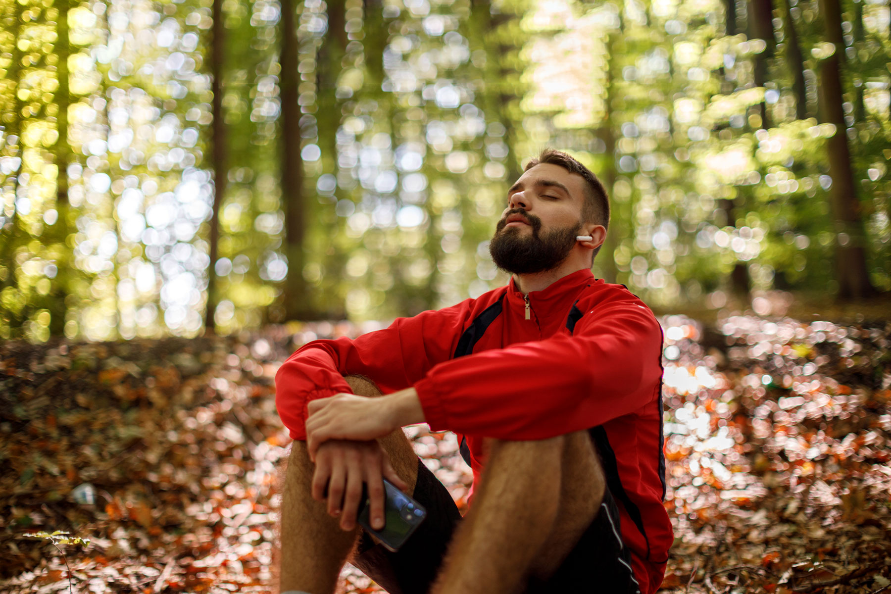 relaxed man sitting in woods holding water bottle and wearing earpods