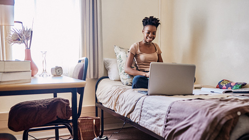 young black woman sitting on her bed in what appears to be a dorm room type area, on her laptop, possibly watching a video or lesson
