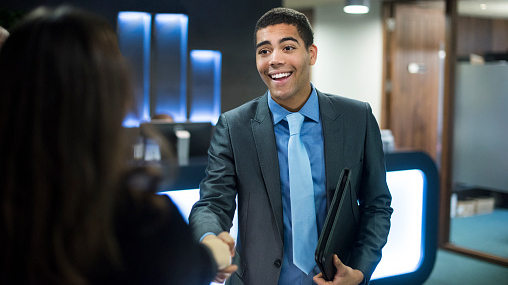excited young man dressed professionally shaking hands, possibly with an interviewer or new boss