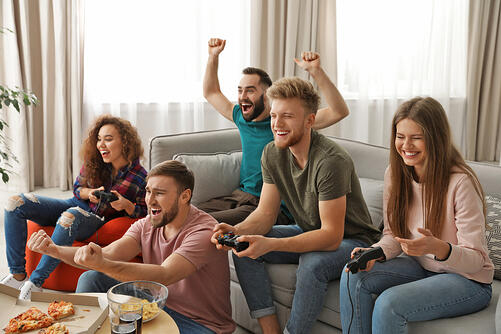 group of friends gathered around couch enthusiastically playing video games