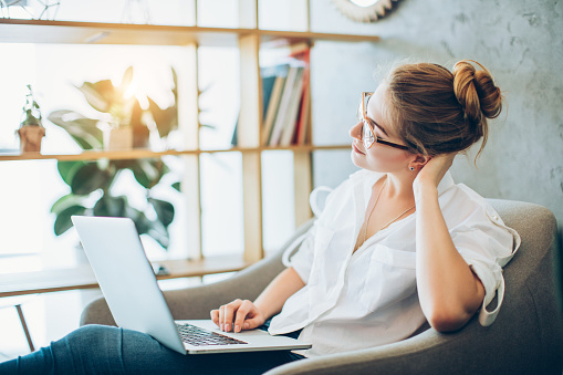 young woman lounding comfortably in a chair working on a laptop