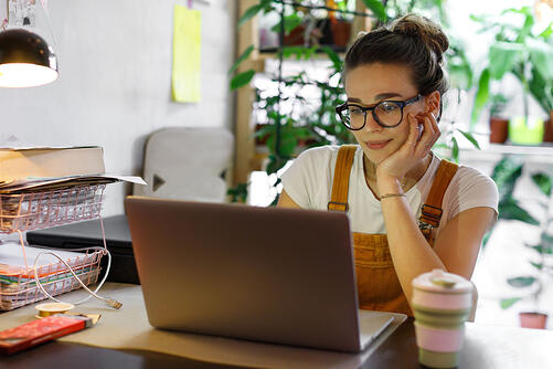 young woman sitting at home on laptop, coffee cup next to her