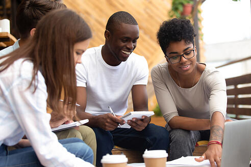 group of diverse college students sitting around a laptop and coffee cups working together