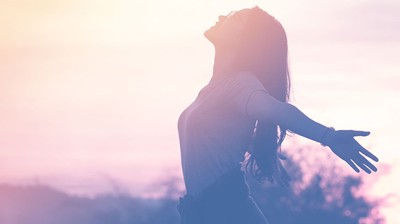 young woman looking up in sky with smile on face and arms out