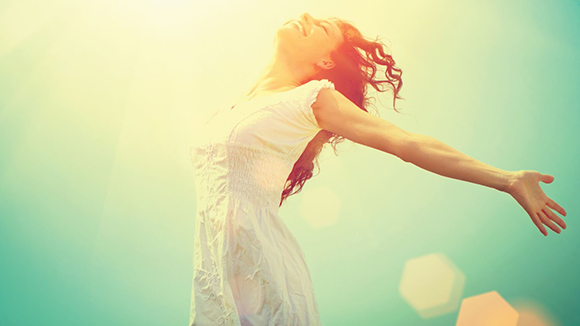 young woman smiling, looking up at sky, arms extended