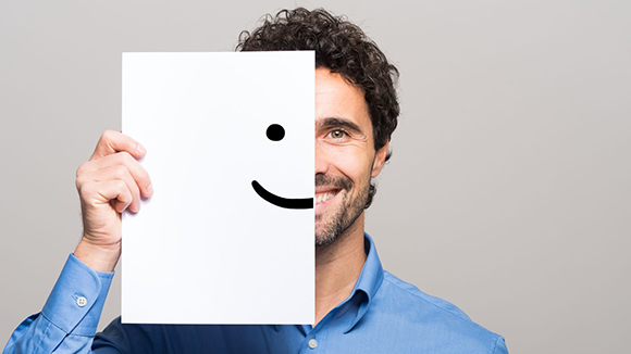 smiling man holding piece of paper in front of his face with half a smiley face