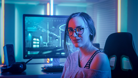 female gamer sits at a desk smiling with a computer behind her