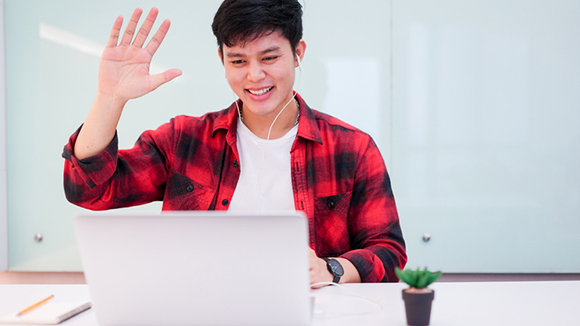 Close up young asian student man wearing earphone and greeting on video conference with friends