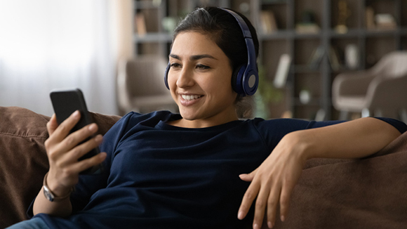 Carefree indian lady wearing headset listen to music from cell