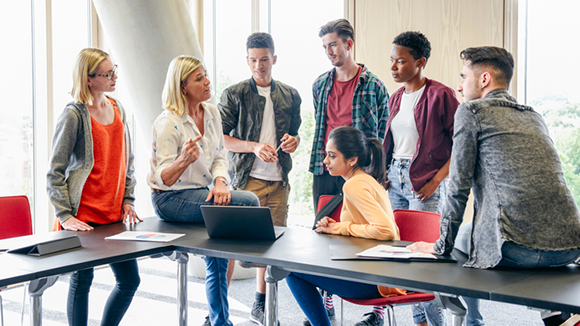 Six college students listening to mature female lecturer with laptop in classroom