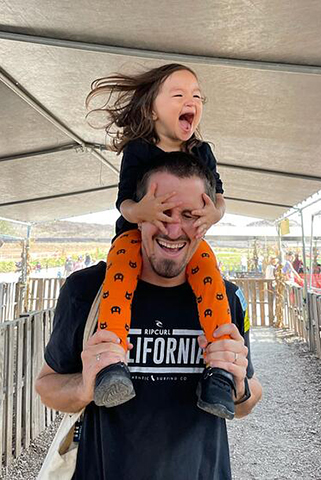 Professor David McDevitt smiles and laughs with his laughing daughter on his shoulders