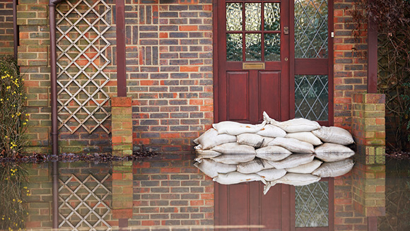 sandbags stacked in front of a front door, water rising in street in front of the residence