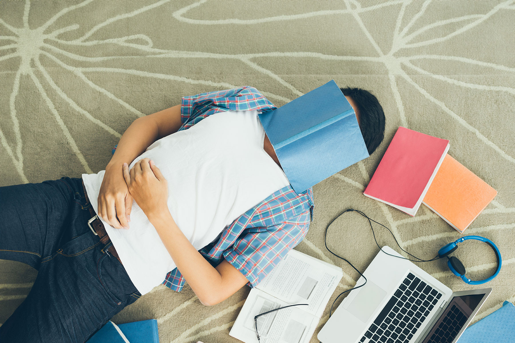 exhausted student laying on floor, book over his face