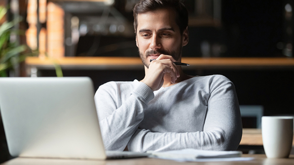 young man pensively sitting in front of a laptop