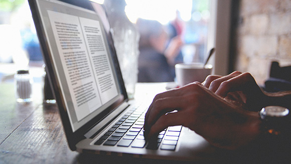 Vintage toned image of man's hands typing on the laptop in the cafe. Finishing a written work, novel or a book while drinking coffee.