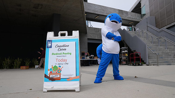 Coastline's dolphin mascot, Fin, stands in front of the food pantry distribution at the Newport Beach campus