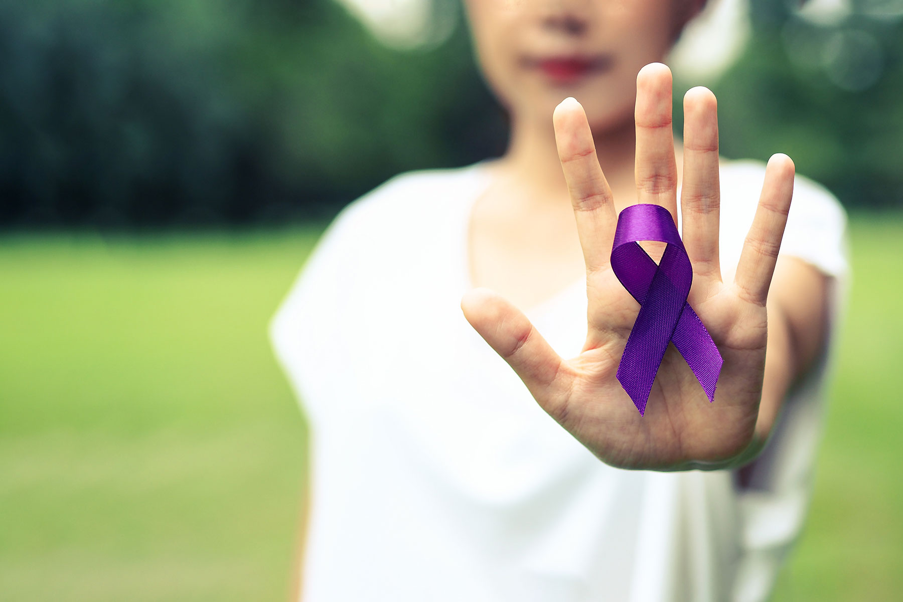 person holding hand up in front of them holding purple ribbon